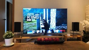 Ein Wohnzimmer mit einem großen Flachbildfernseher, der einen Netflix-Film zeigt, einem Couchtisch aus Holz mit roten Äpfeln, einer weißen Topfpflanze und zwei Lautsprechern.