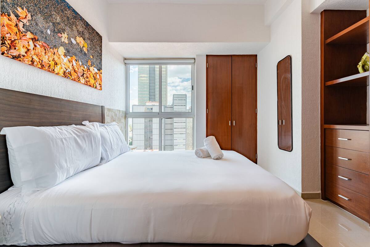 Ein modernes Hotelzimmer mit einem großen Bett, einem Holzschrank und Blick auf die Stadt.