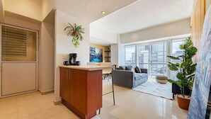 A modern living room with a sofa, a coffee table, and a dining area. There is a large window providing a view of the city. - Anahuac Apartments by VH (Mexico City)