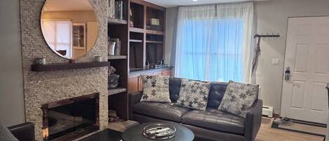 A modern living room with a fireplace, a round mirror, a sofa, and a coffee table.