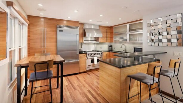 Una cocina moderna con armarios de madera, electrodomésticos de acero inoxidable y una isla central con taburetes de bar.
