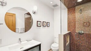 Un baño moderno con un espejo redondo, lavamanos blanco y una ducha con mosaicos.