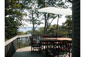 Relax on the balcony with a view of the water and trees, surrounded by a shaded seating area with a table and chairs.