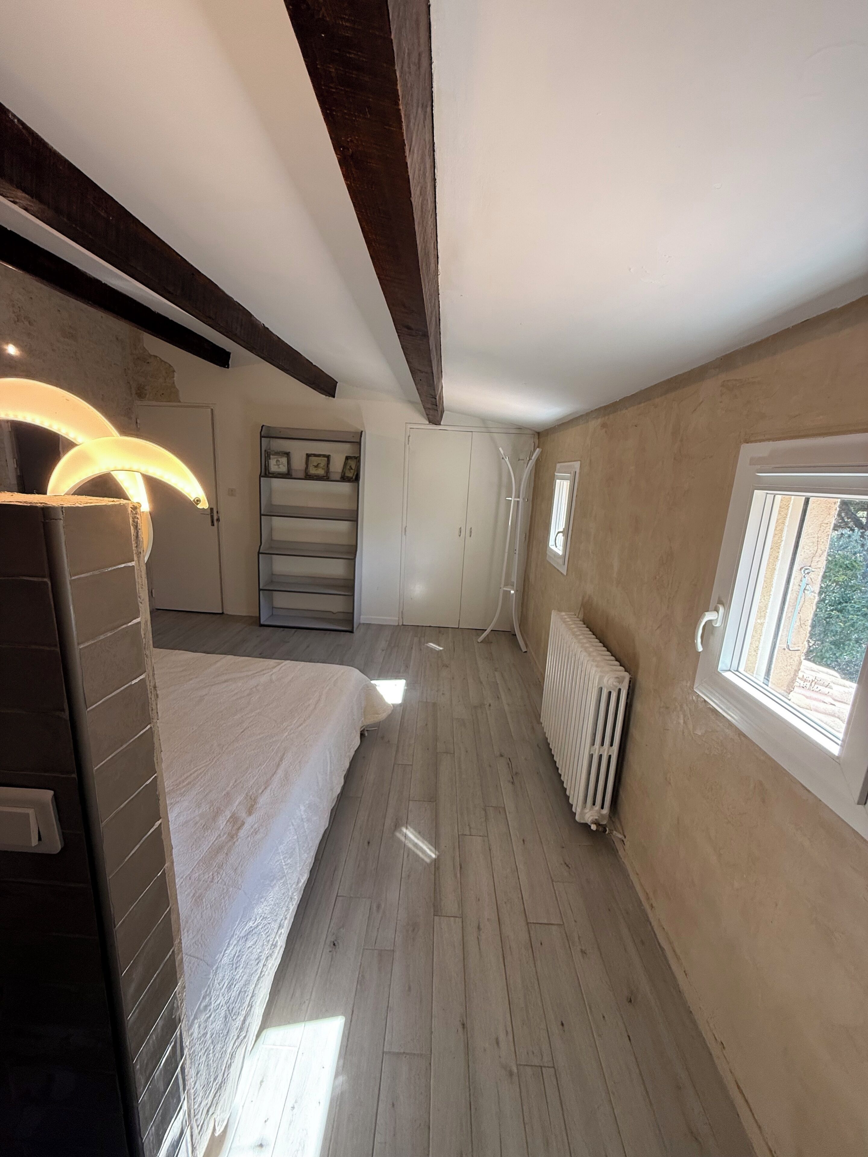 A bedroom with a bed, a radiator, a window, and a wardrobe.