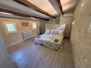 A bedroom with a bed, wooden beams, a radiator, and a window.
