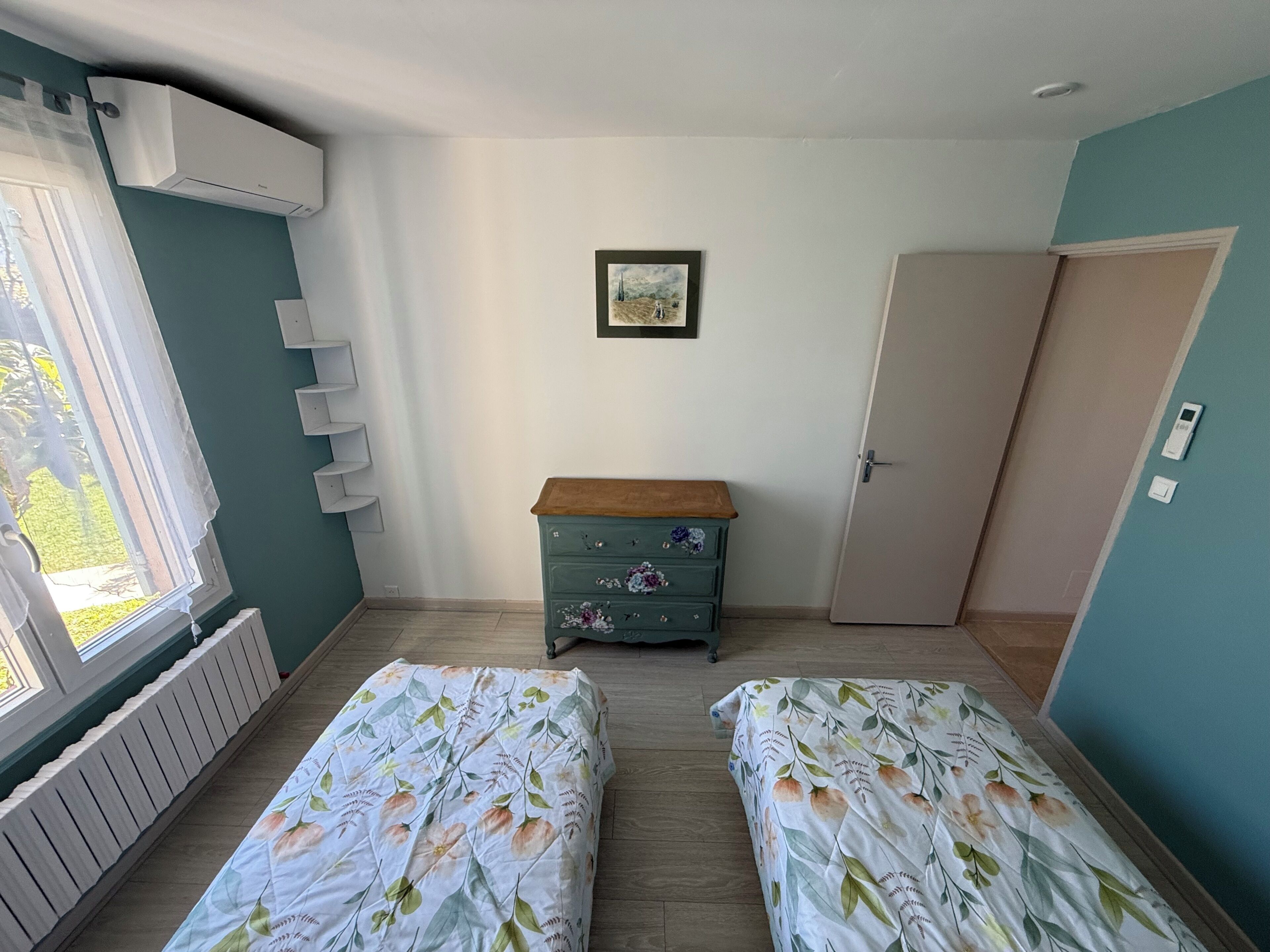 Une chambre avec deux lits, une commode, un radiateur, une porte et une fenêtre.