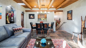 A spacious living room with a leather sofa, a dining area with a wooden table and chairs, and a staircase leading to another level. - El Corazon - Walking Distance to the Plaza (Santa Fe)