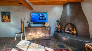 A living room with a fireplace, a television, and a rustic wooden ceiling. - El Corazon - Walking Distance to the Plaza (Santa Fe)