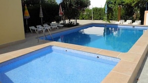 Una piscina rectangular con borde de azulejos, rodeada de sillas de descanso y sombrillas.