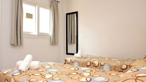 Habitación de hotel con dos camas, una ventana con cortinas, un espejo y una colcha estampada.