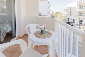 Un balcone con tavolo e sedie bianche, un vaso con fiori e vista sulla città.