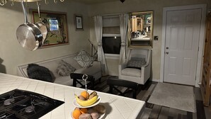 Una cucina con piano cottura a gas, un tavolo da pranzo con della frutta, un divano, una sedia e una ventola a soffitto.