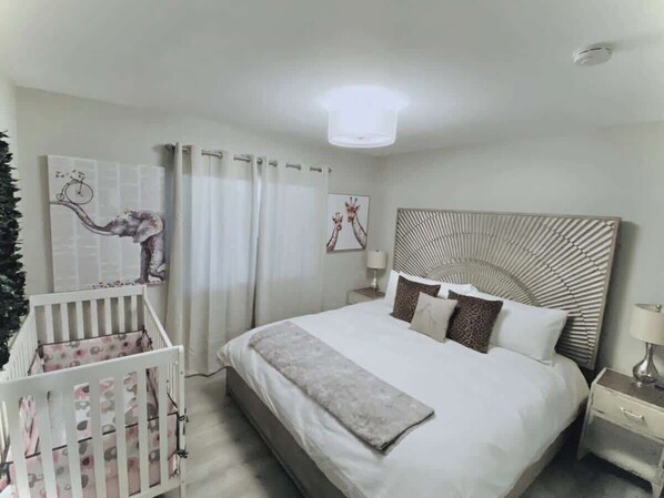 Un dormitorio con cama, cuna, mesita de noche y lámpara de pared.