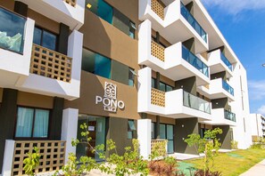Un hôtel moderne, reconnaissable à son grand panneau « PONO », doté de nombreux balcons et d’un jardin bien entretenu.