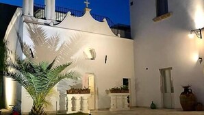 Un patio con un edificio blanco que cuenta con una torre de campanas y una cruz, rodeado de un pavimento de piedra.