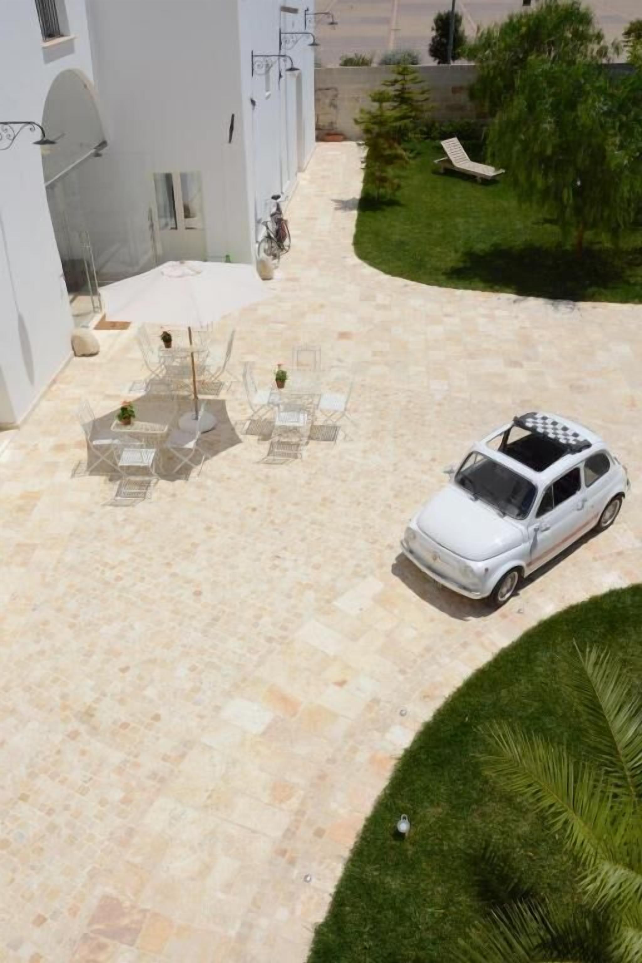 A courtyard with a white car parked on the right, surrounded by a paved area with outdoor furniture.