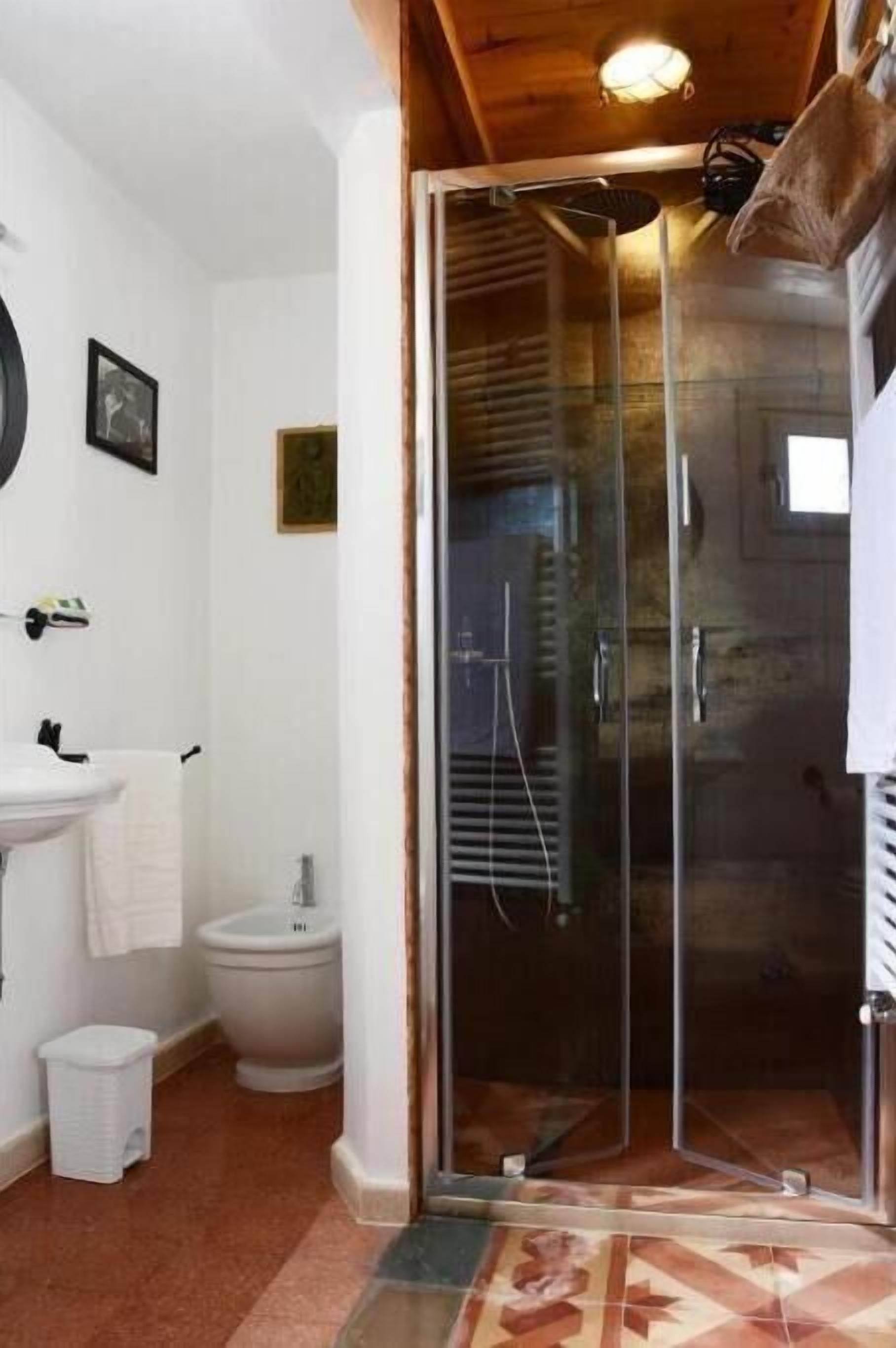 Un bagno con box doccia in vetro, lavandino, water e un piccolo cestino.