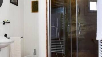 Un bagno con box doccia in vetro, lavandino, water e un piccolo cestino.