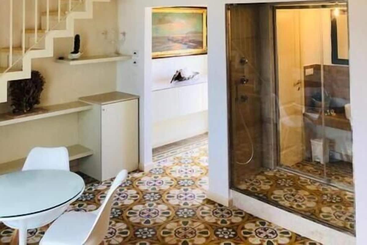 A staircase with a railing leading to a second floor, a dining area with a table and chairs, and a shower area with a glass door.