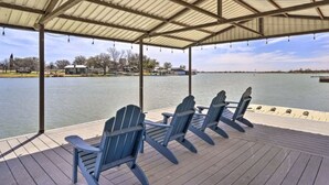 Una terraza techada con cuatro sillas Adirondack mirando hacia un lago.
