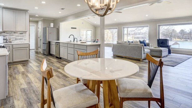 Una cocina amplia con una mesa redonda y sillas de comedor, un candelabro moderno y vistas al exterior.