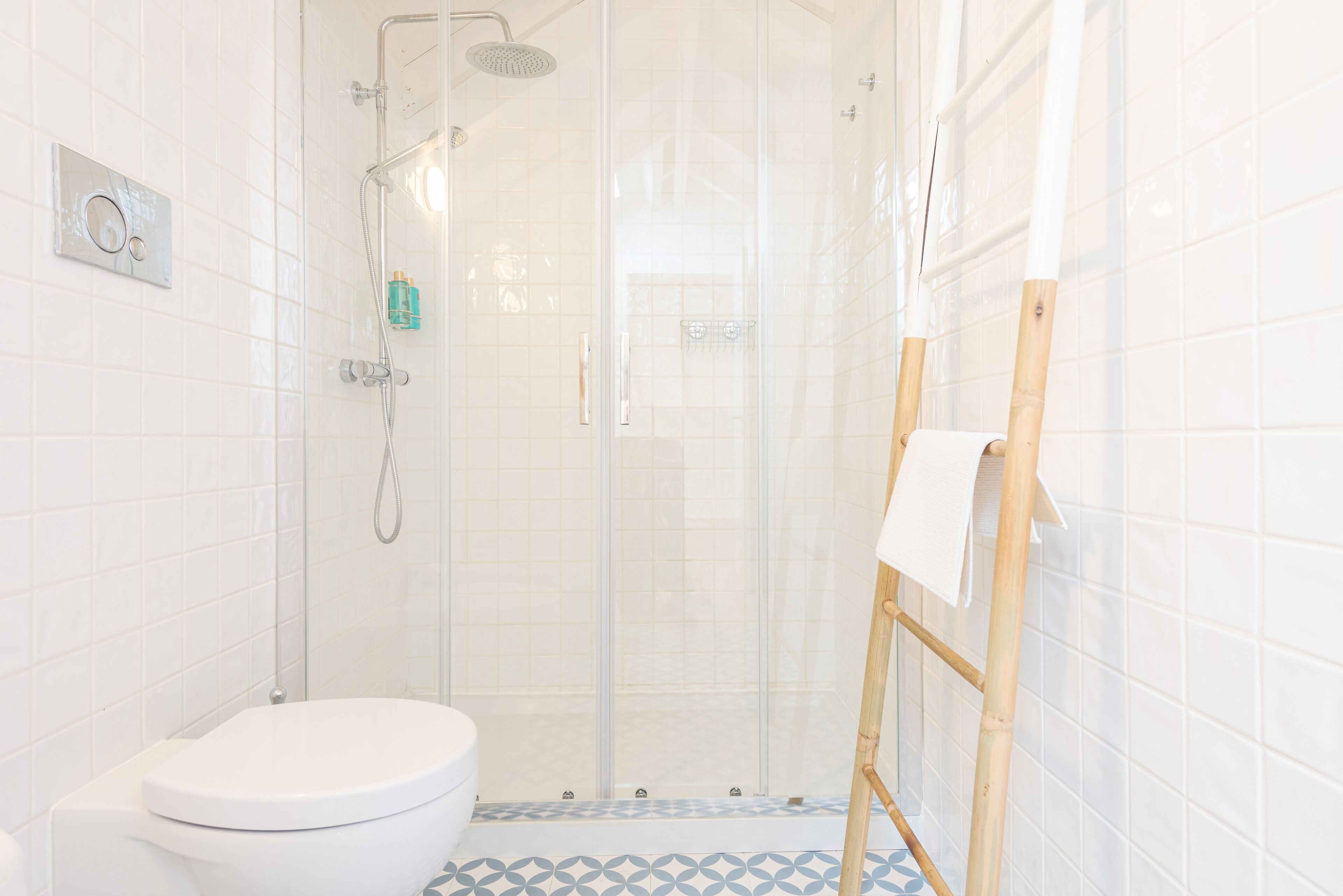 Baño con inodoro, ducha y un caballete de madera con una toalla.