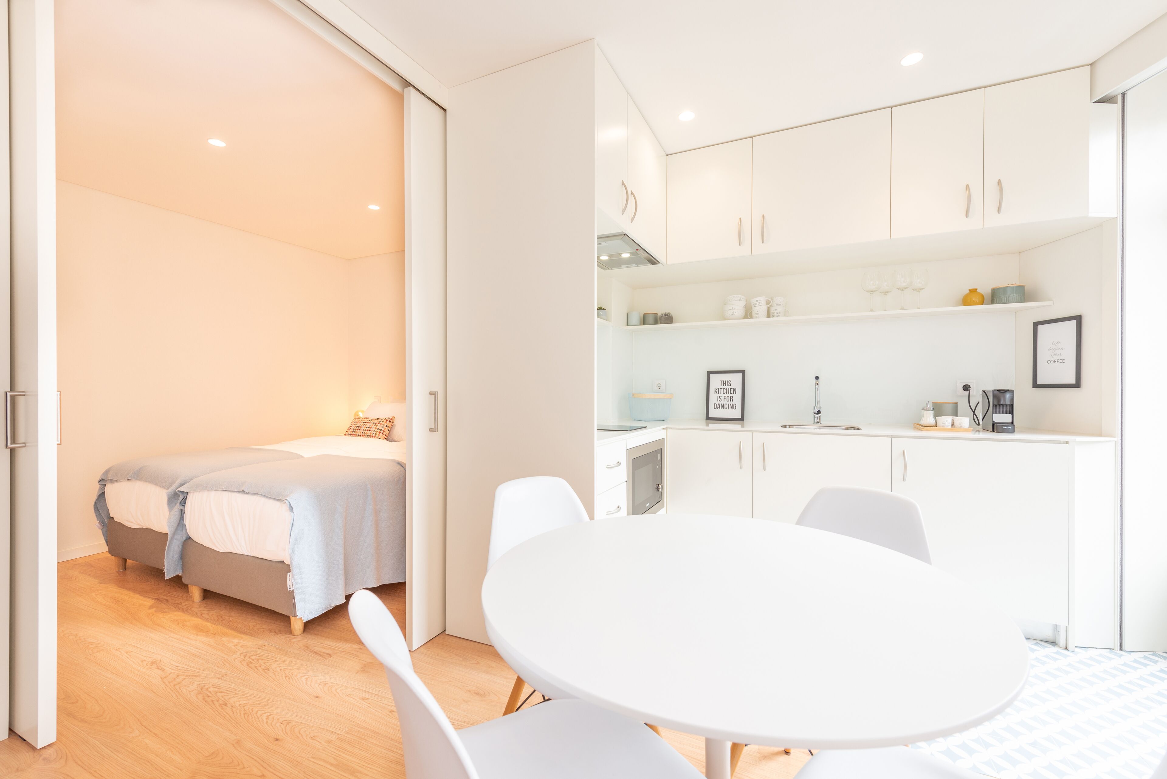 Een moderne, goed verlichte kamer met een bed, een eettafel en een kitchenette.