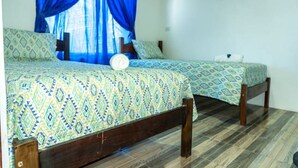Dos camas individuales con ropa de cama estampada, un cabecero de madera y una ventana con cortinas azules.