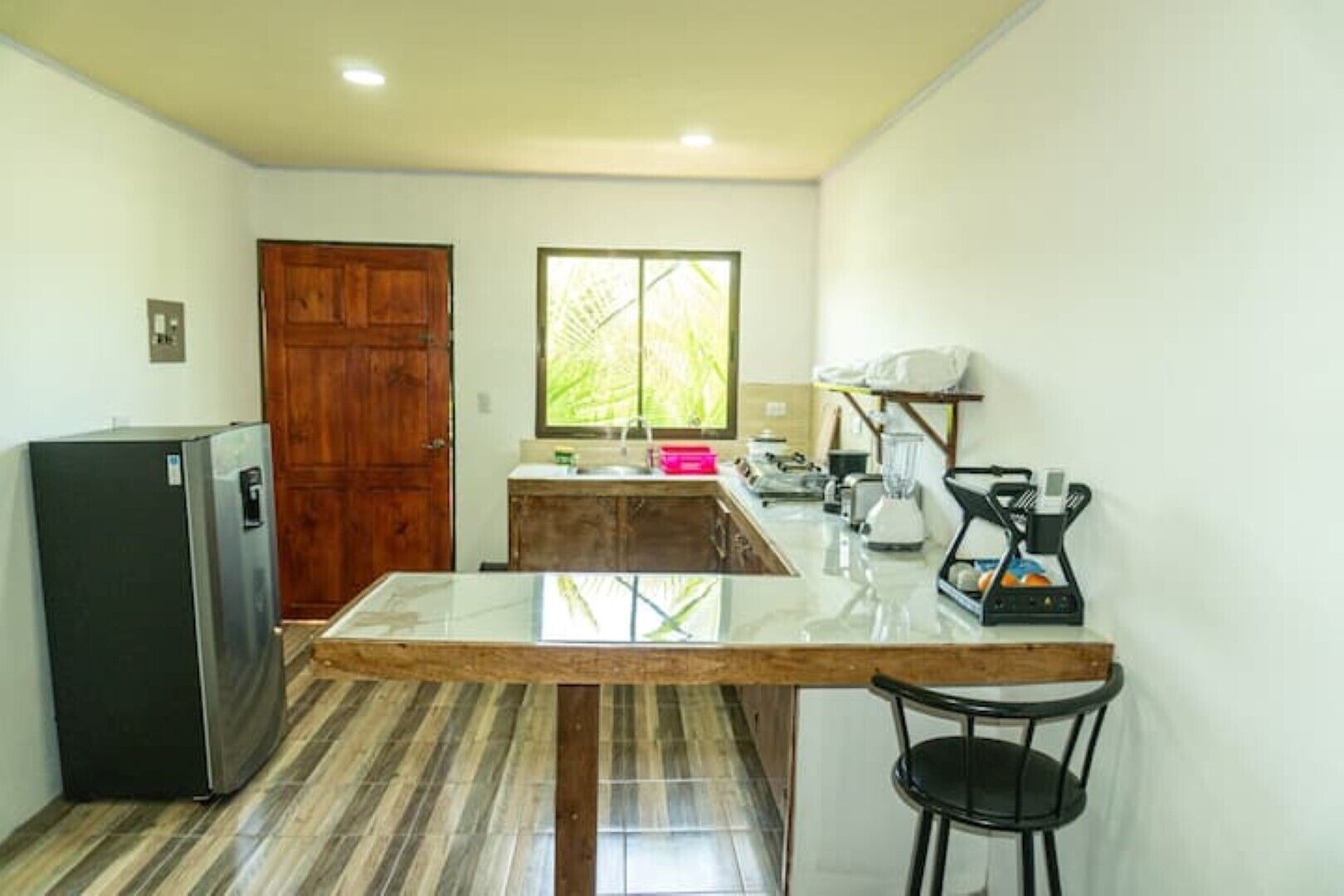 A compact kitchen with a refrigerator, wooden cabinets, a countertop, a sink, and a window.
