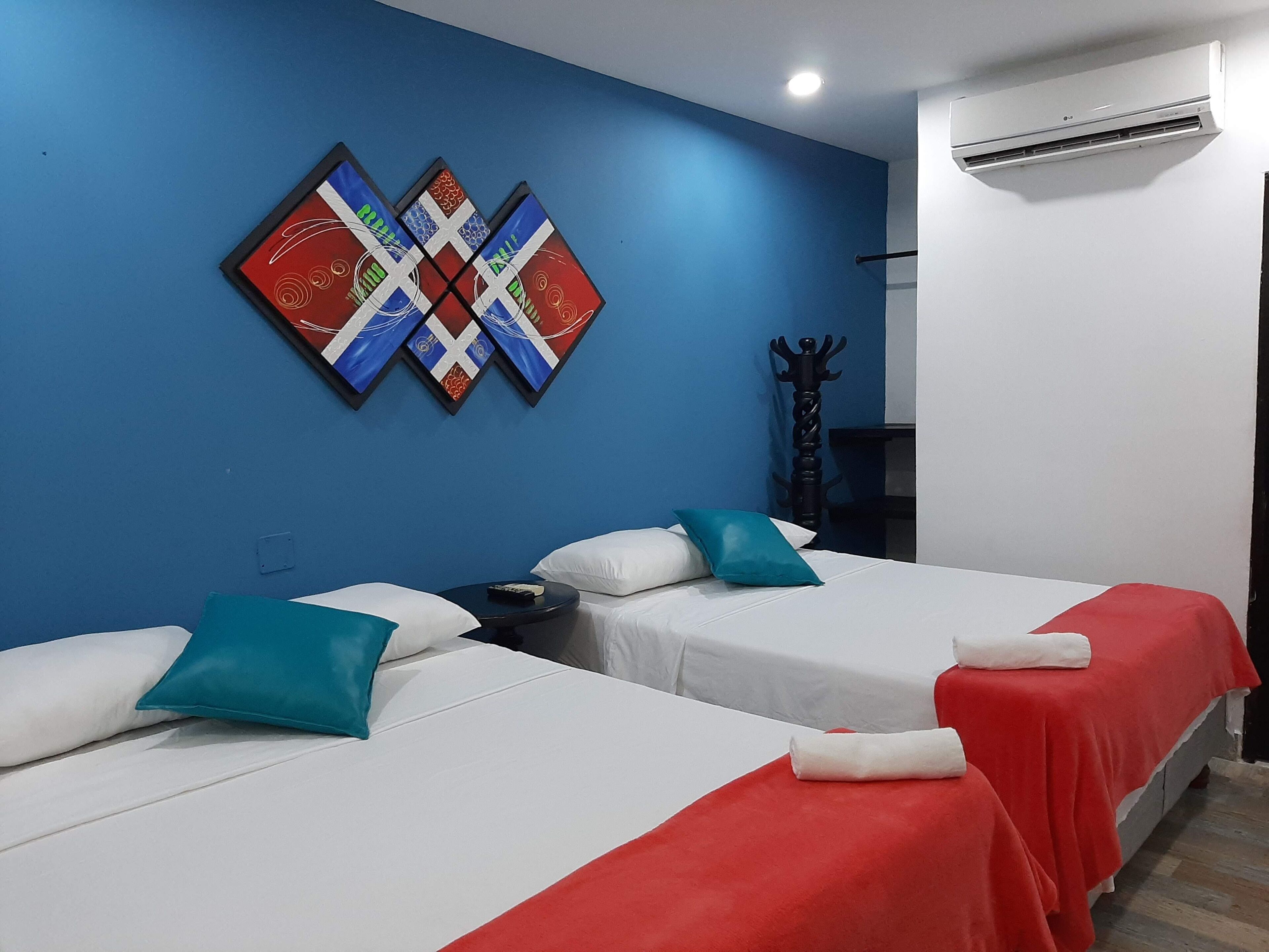Habitació d'hotel amb dos llits, una paret blava i un edredó vermell.