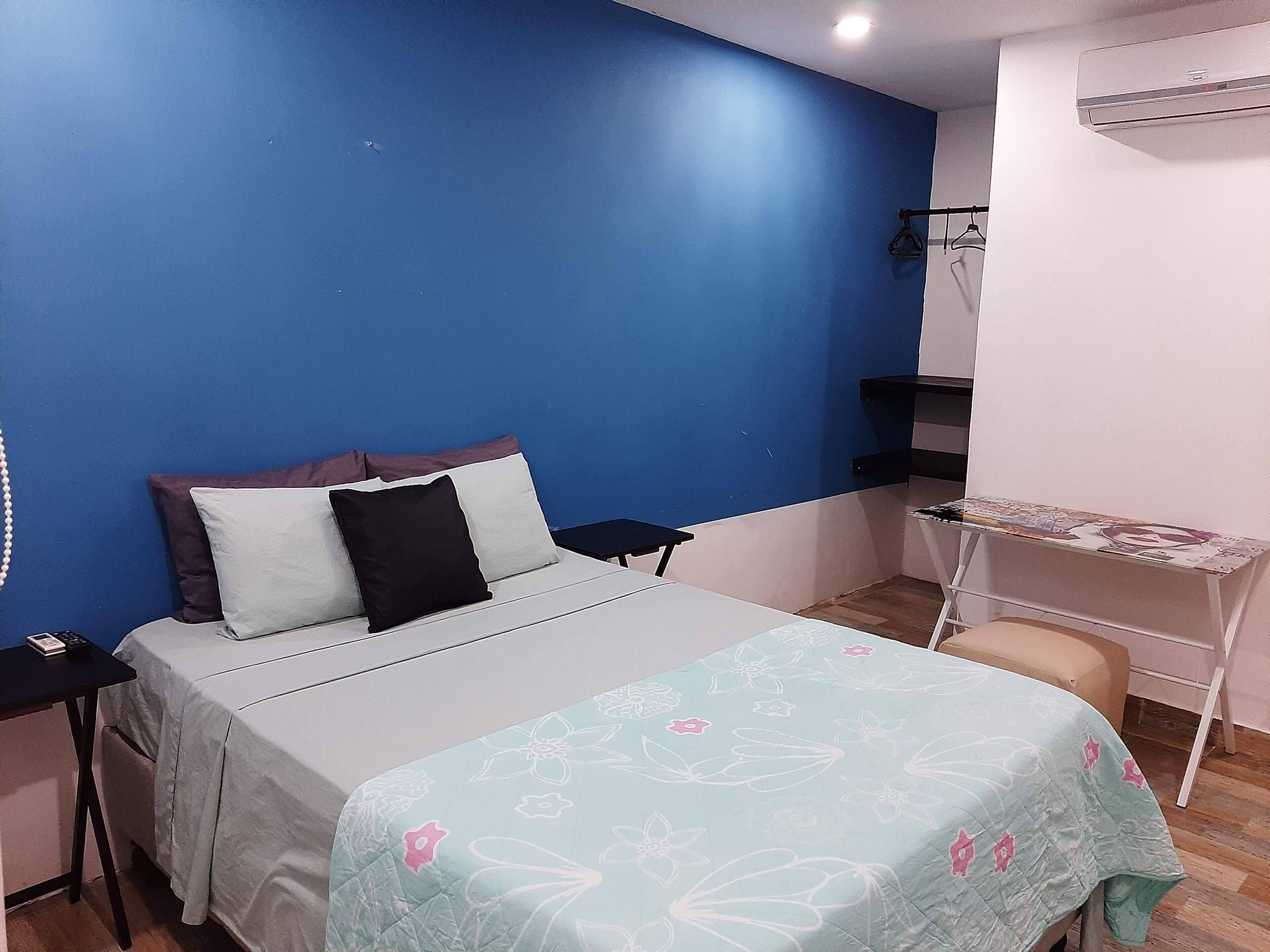 A bedroom with a bed, a desk, and an air conditioning unit.