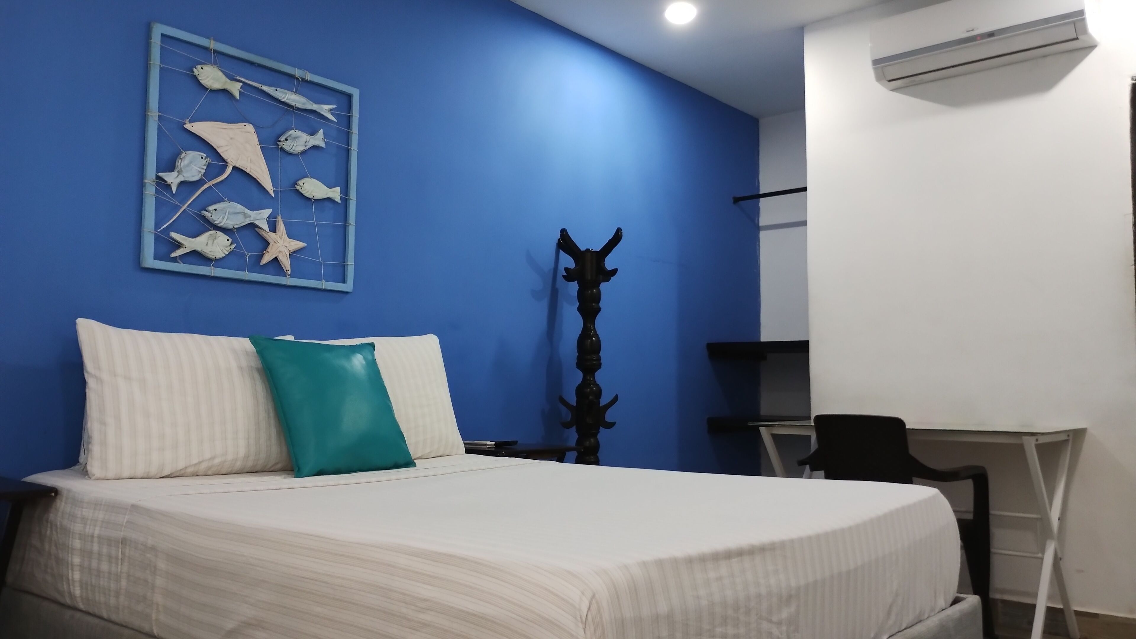 A bedroom with a bed, pillows, a desk, and a wall-mounted air conditioner.