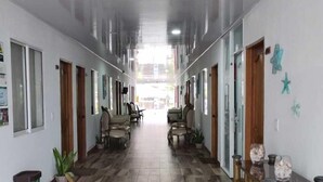 A hallway with wooden flooring, chairs, a trash bin, and decorative items on the walls. - HOTEL SUNSET BEACH (Cartagena)