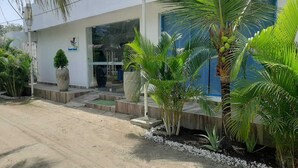 A building with a white exterior, a blue door, and a small garden with palm trees and a large planter. - HOTEL SUNSET BEACH (Cartagena)