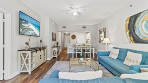 A spacious living room with a blue sofa, a coffee table, and a TV mounted on the wall. - First Floor Condo • Walk to Beach • Sleeps 4 (Mexico Beach)