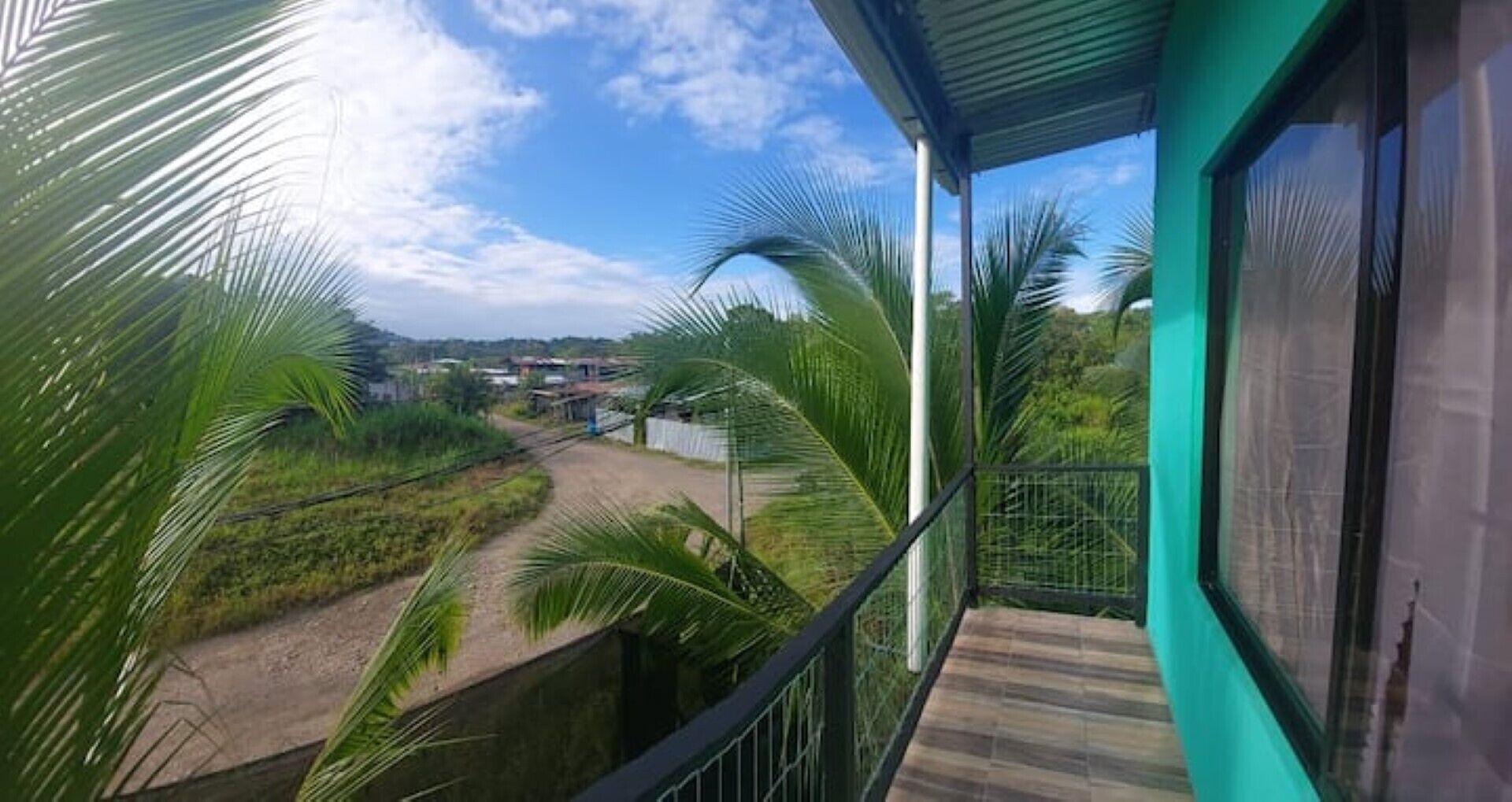 A balcony with a view of a rural landscape, including palm trees and a dirt road.