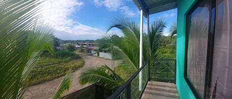 A balcony with a view of a rural landscape, including palm trees and a dirt road.