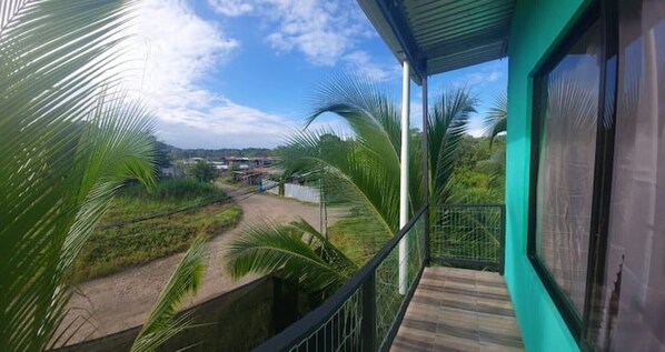 Un balcón con vistas a un paisaje rural, que incluye palmeras y un camino de tierra.