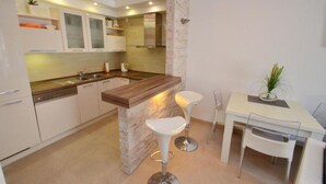 A modern kitchen with white cabinets, a wooden countertop, and two bar stools. - Muo Apartments (Kotor)