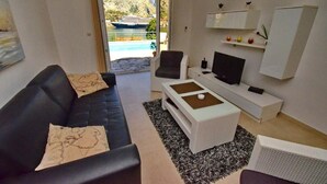 A modern living room with a black leather sofa, a white coffee table, and a television. There is a view of a body of water and a ship in the background. - Muo Apartments (Kotor)