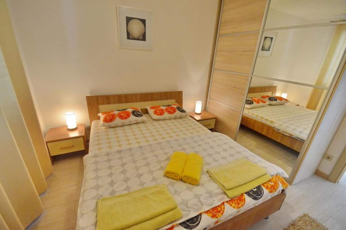 A neatly made bed with a patterned bedspread, two bedside lamps, and a mirror reflecting the room.