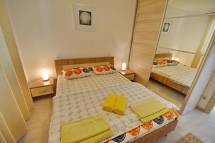 Una cama bien hecha con una colcha estampada, dos lámparas de noche y un espejo que refleja la habitación.