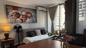 A hotel room with a bed, a desk, a fan, a lamp, a painting, and a window with curtains. - VR Suite (Santiago)