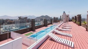 A rooftop pool area with lounge chairs and a clear view of the city and mountains in the background. - VR Suite (Santiago)
