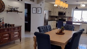 A modern kitchen with a dining area, featuring a wooden table, blue upholstered chairs, and a chandelier.