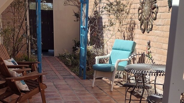 A patio area with terracotta tiles, a blue pergola, and outdoor furniture including a wicker chair and a metal table.