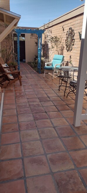 A patio area with terracotta tiles, a blue pergola, and outdoor furniture including a wicker chair and a metal table. - Historic Old Spanish Trail Location with Stunning Views and Pathways (Tucson)
