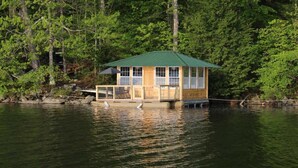 A wooden cabin with a green roof on stilts over water, surrounded by dense forest.