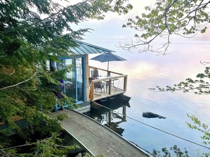 A floating house with a glass door, a deck with outdoor furniture, and a view of the water.