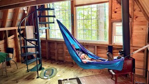 Een houten cabin met een hangmat, een spiltrap en grote ramen.